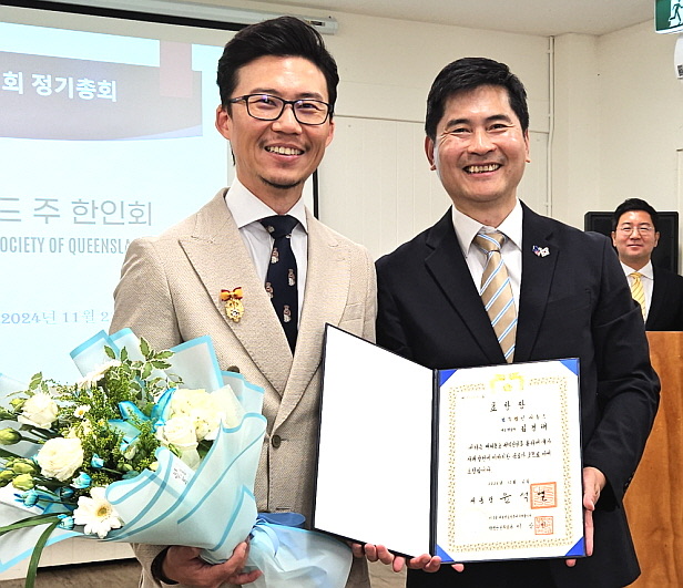 Tenny Kim holding the Republic of Korea Presidential Commendation certificate alongside the presenting official, 2024